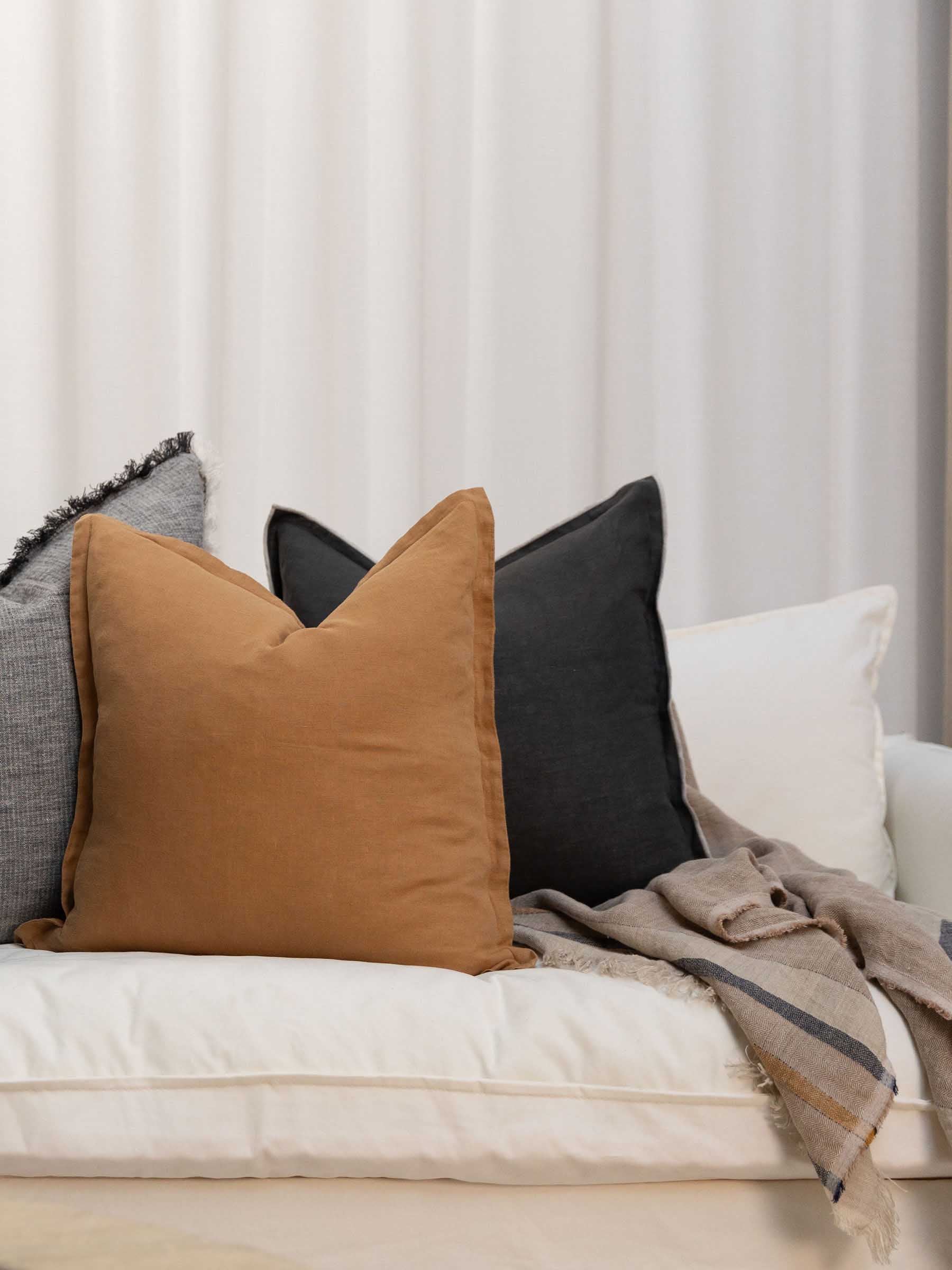 Arlo french flax linen sand dune throw draped over sofa in a living room showcasing herringbone weave pattern fringed edged and contrasting stripes