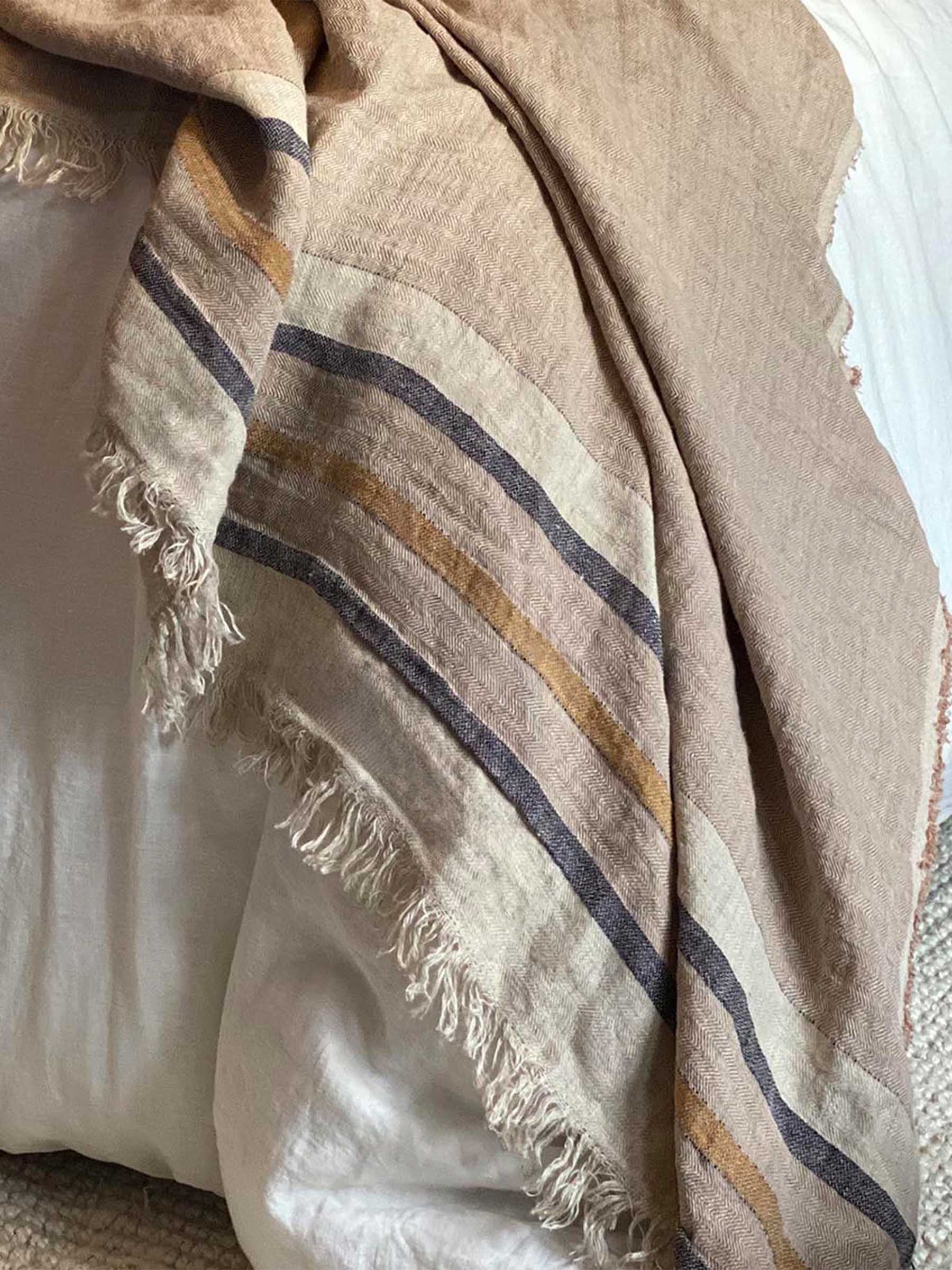 Close up detail of Arlo sand dune french flax linen throw layered on bed with herringbone weave contrasting stripe and fringed edges