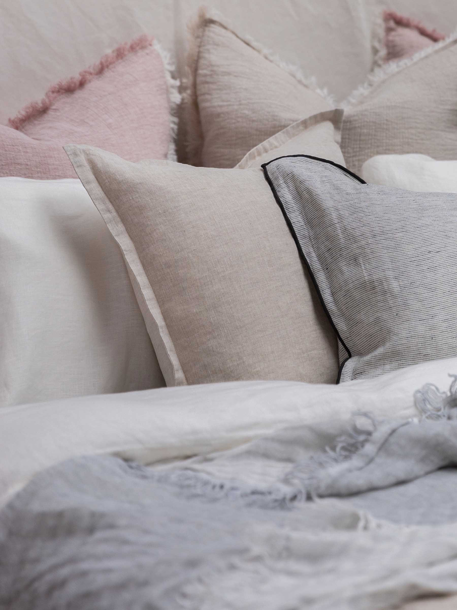 Close up detail of Felix French Flax linen cushion in Natural colour with flanged border layered on bed with neutral bedding