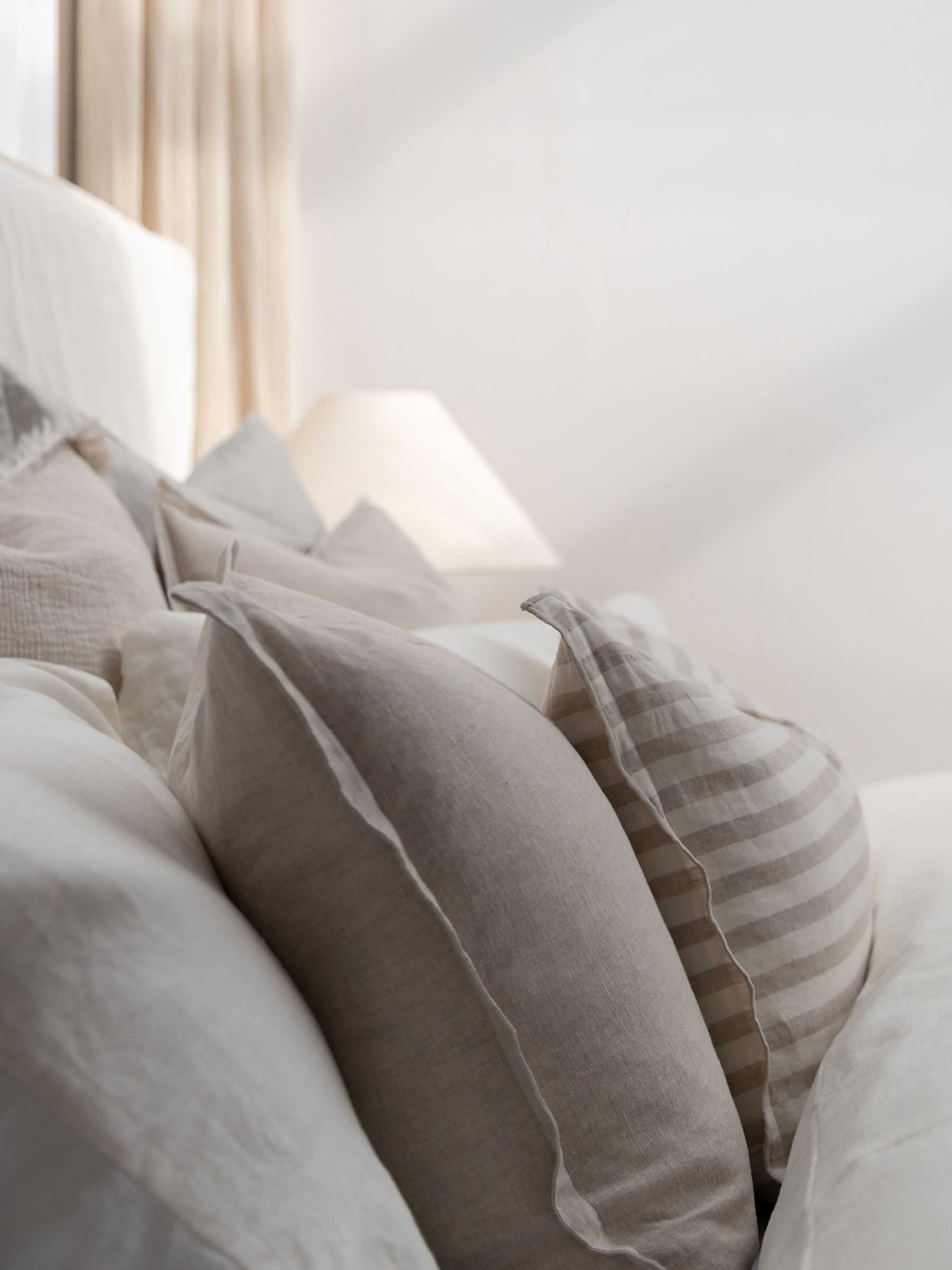 Close up detail of Felix French Flax linen cushion in Natural colour showing flanged border styled on neutral bed in bedroom setting