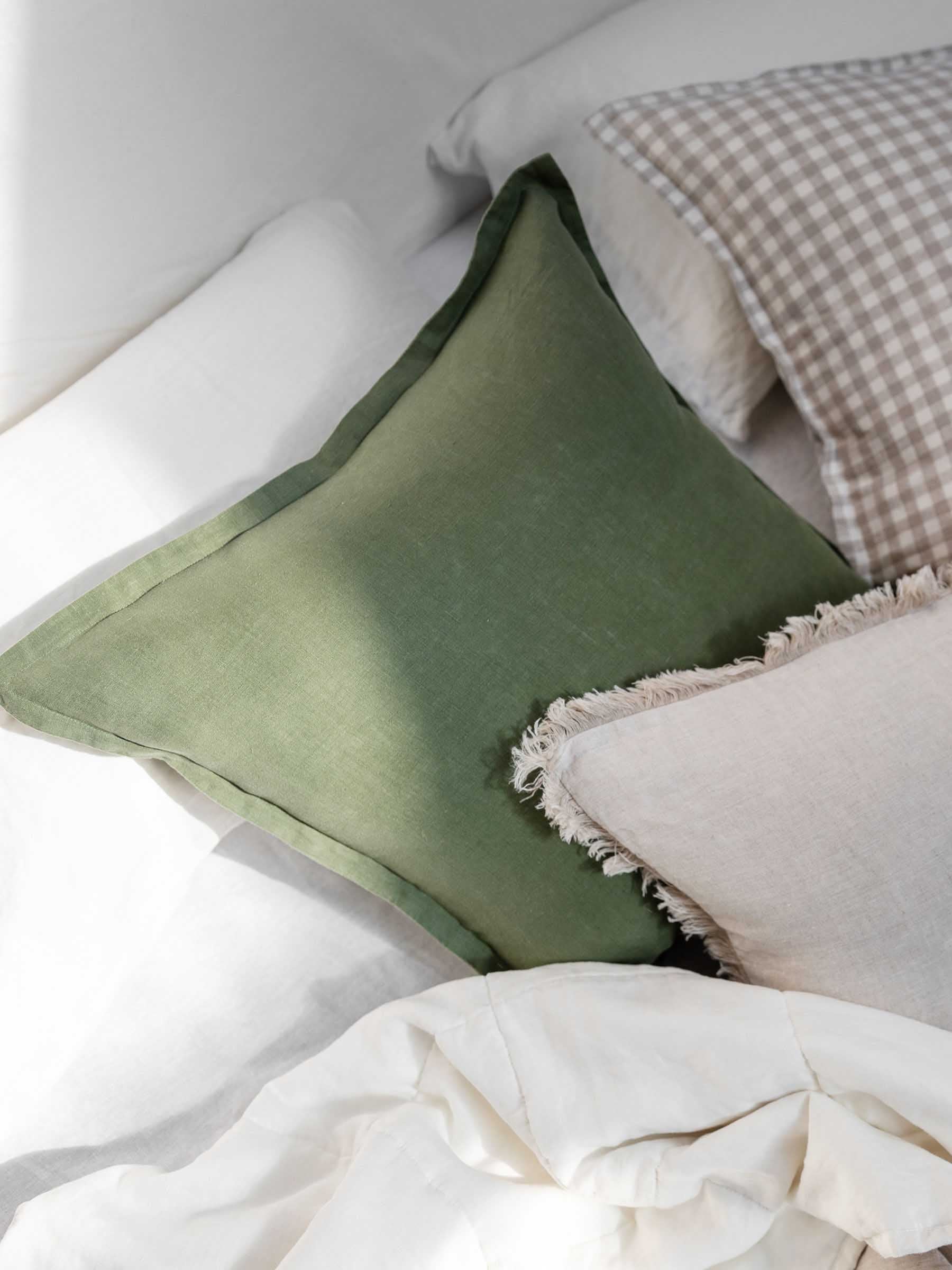 Close up of Felix Basil green cushion on bed setting showing french flax linen material and flanged border