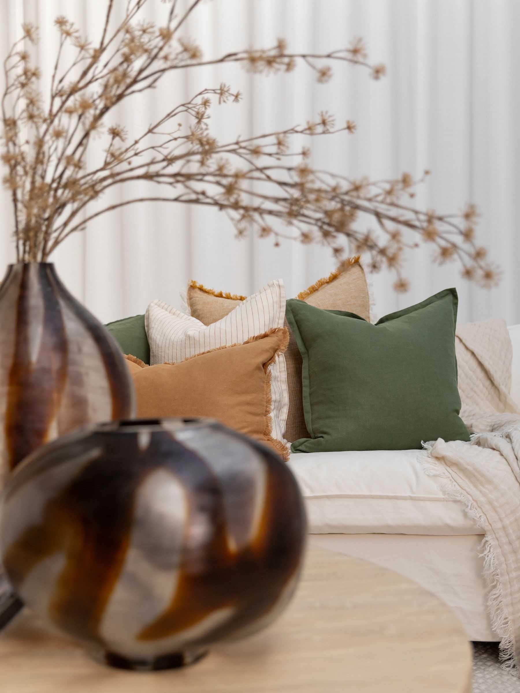Felix French Flax linen cushion in 50cm square Basil green styled on sofa in modern living room setting
