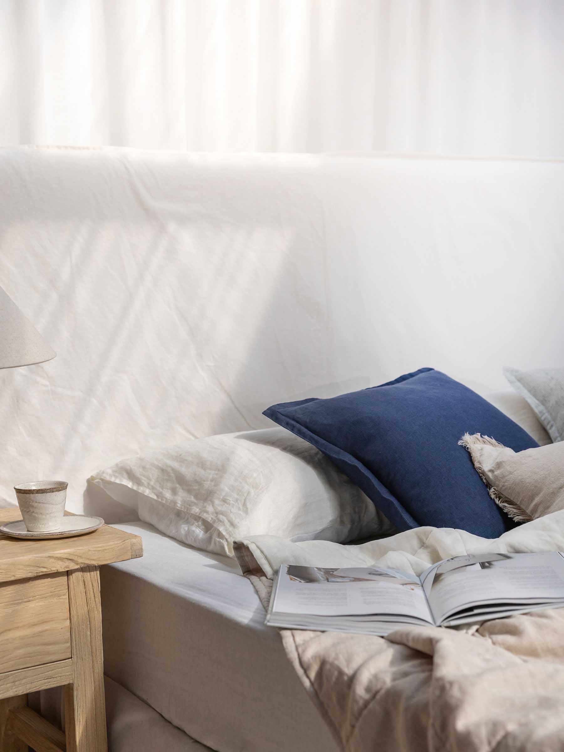Felix 50cm square Navy French Flax linen cushion with flanged border displayed on bed with white bedding in coastal bedroom setting