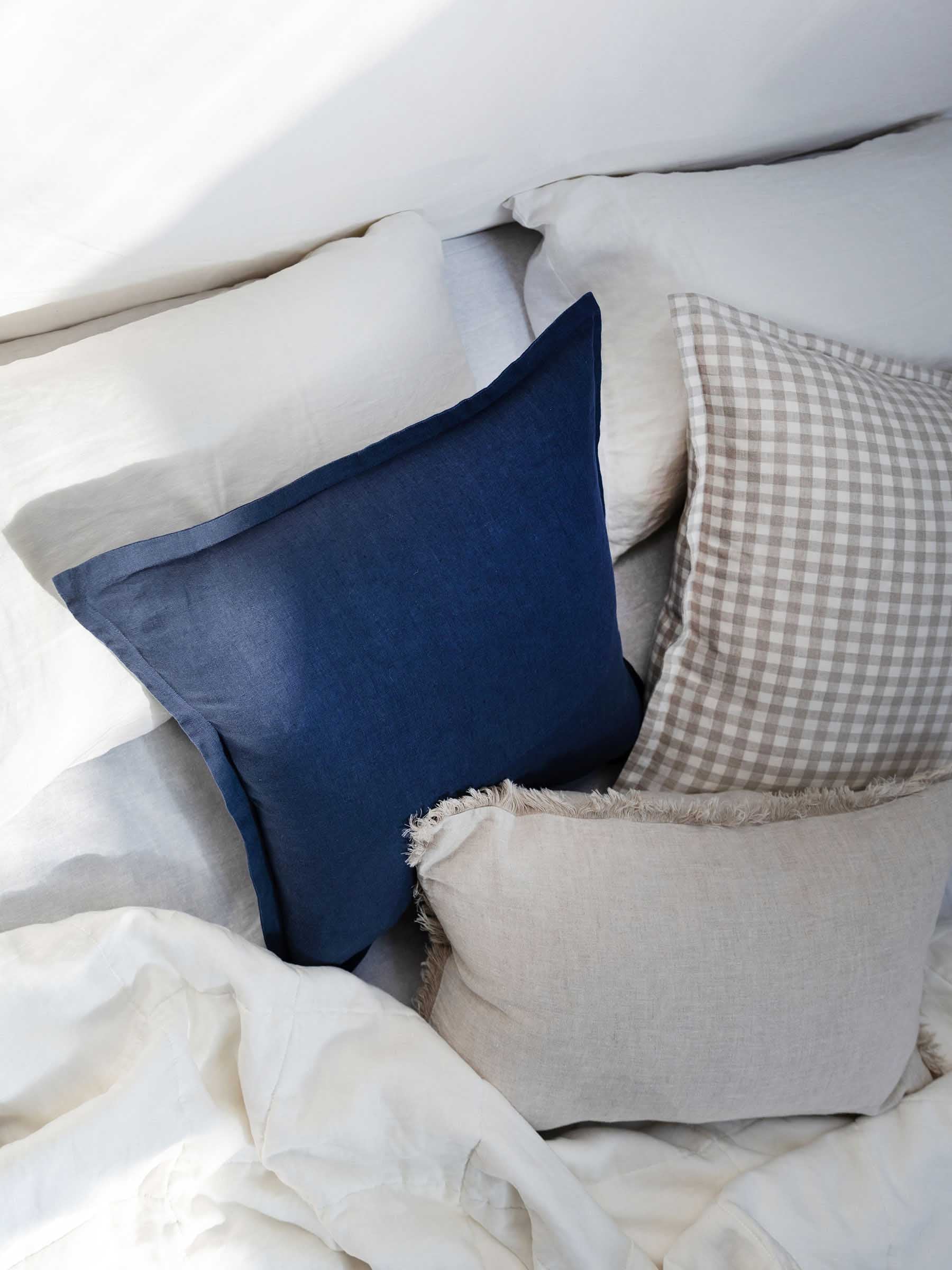 Close up detail of Felix French Flax linen cushion in Navy colour with flanged border on bed setting with stacked cushions