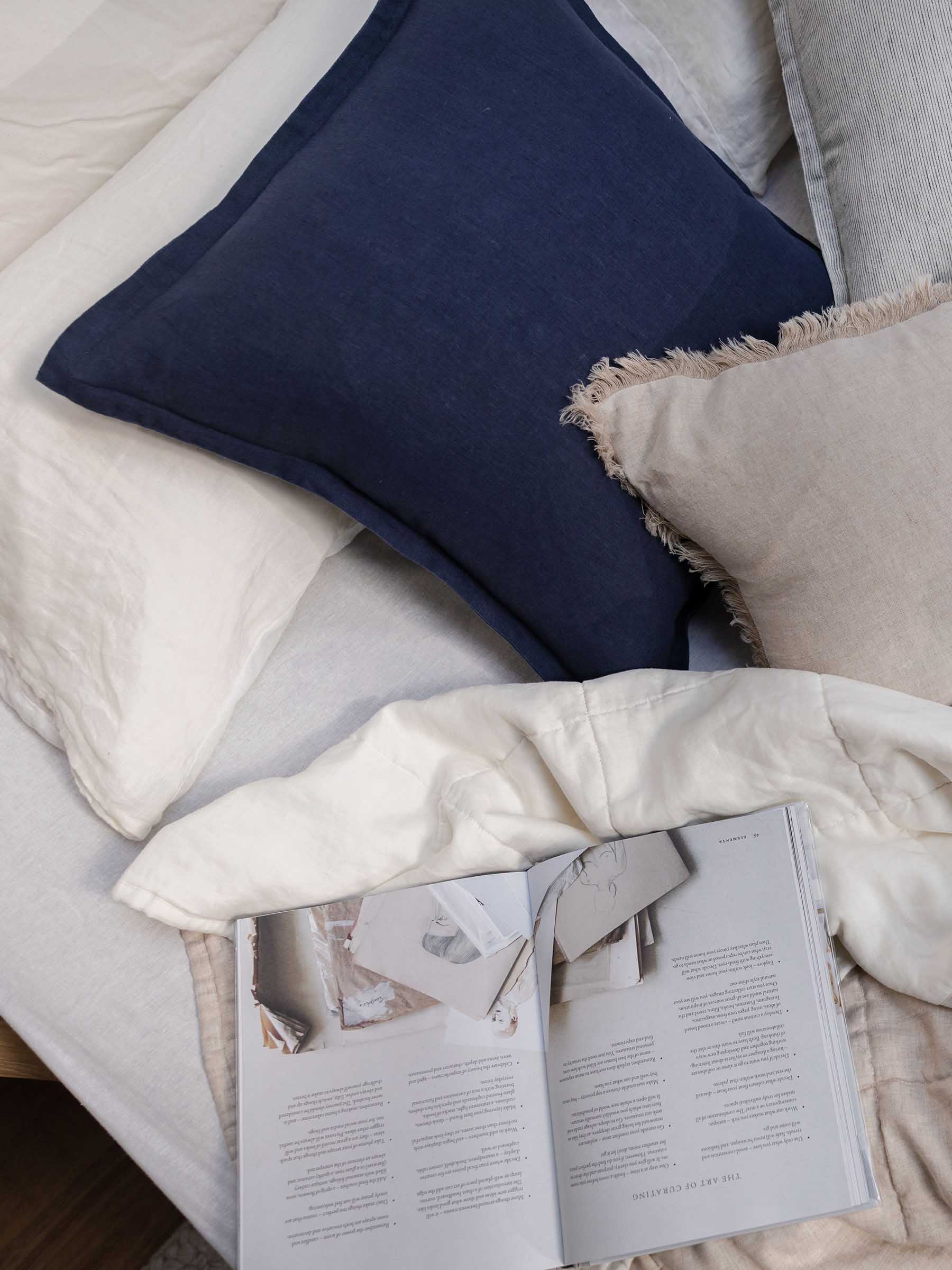 Close up detail of Felix French Flax linen cushion in Navy colour with flanged border on bed setting with neutral bedding