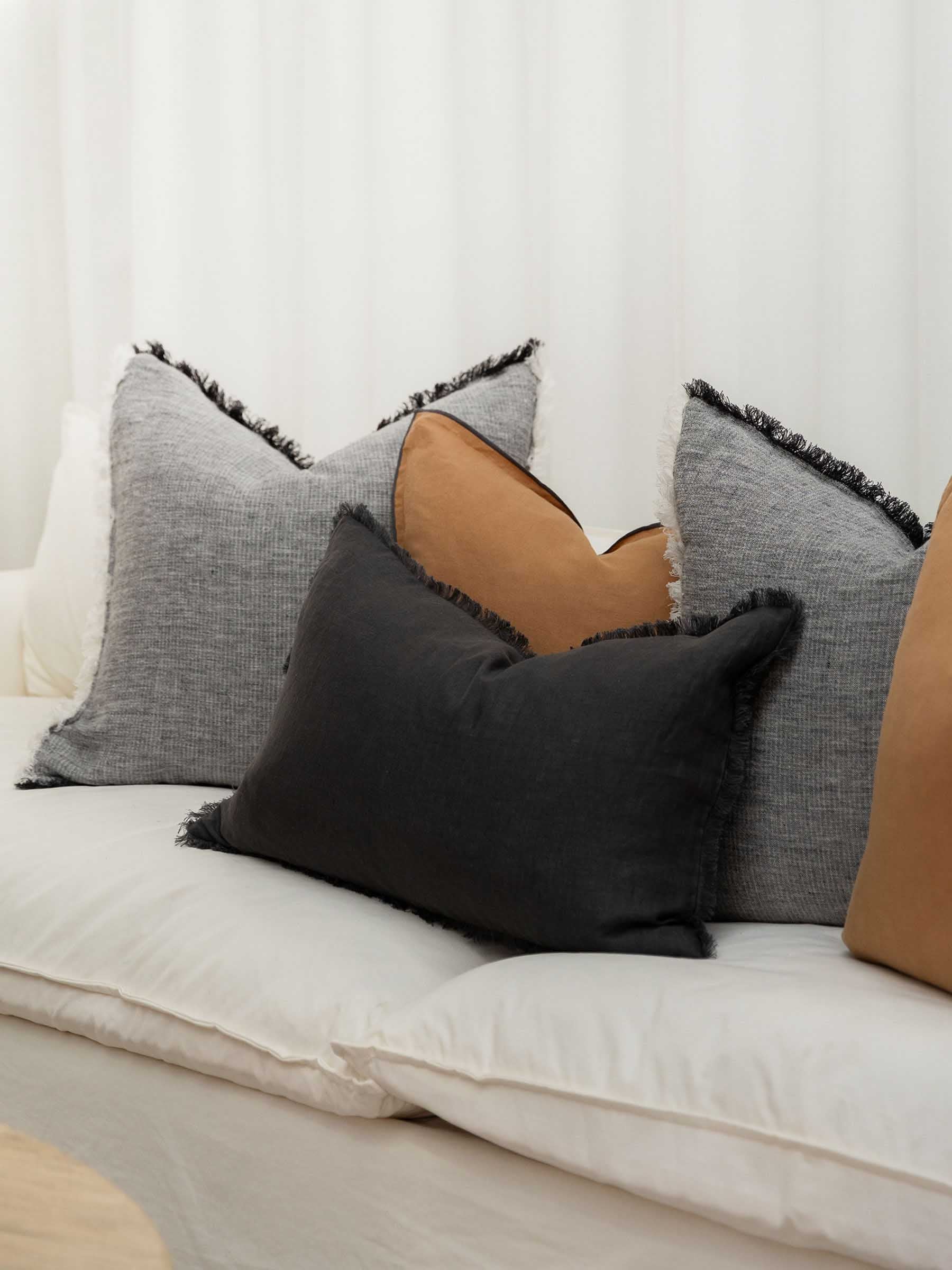 Harlow French Flax linen cushion in Butterscotch colour 50cm square with graphite overstitching trim styled on sofa in modern living room setting