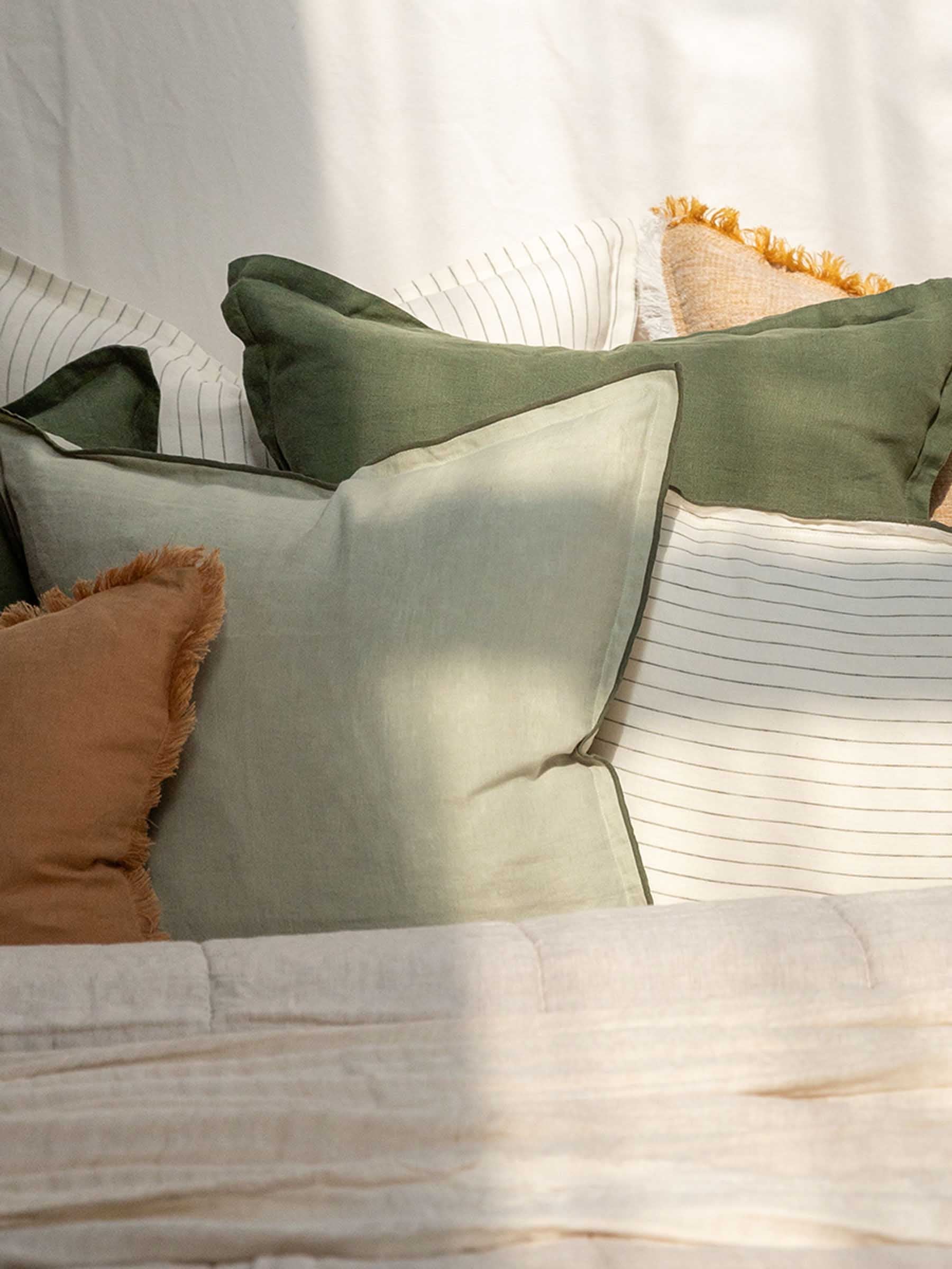 Close up detail of Harlow French Flax linen cushion in Gumleaf colour showing basil overstitching trim on bed setting with stacked linen cushion