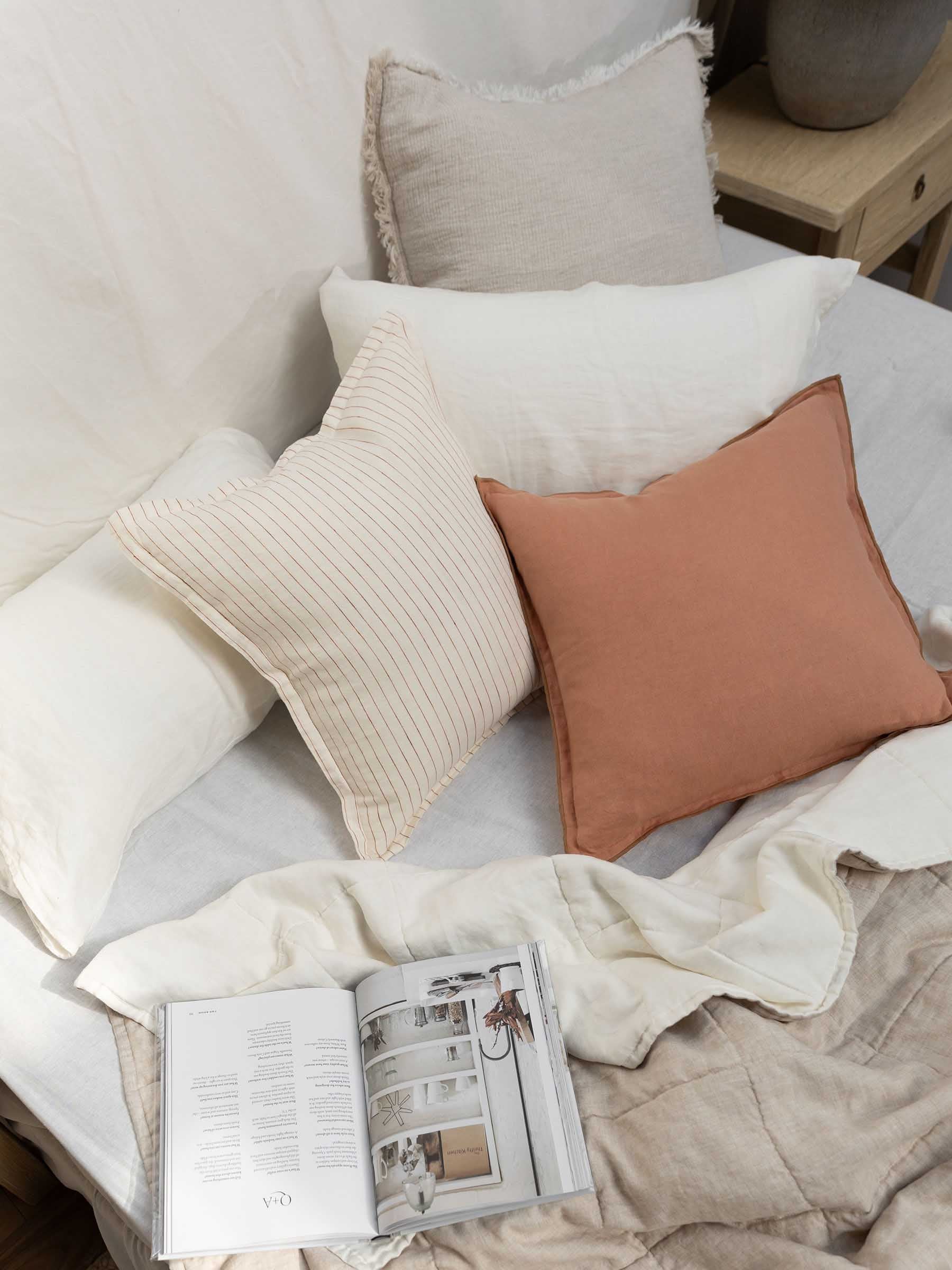 Harlow French Flax linen cushion in Clay colour with butterscotch overstitching trim styled on bed with neutral bedroom setting