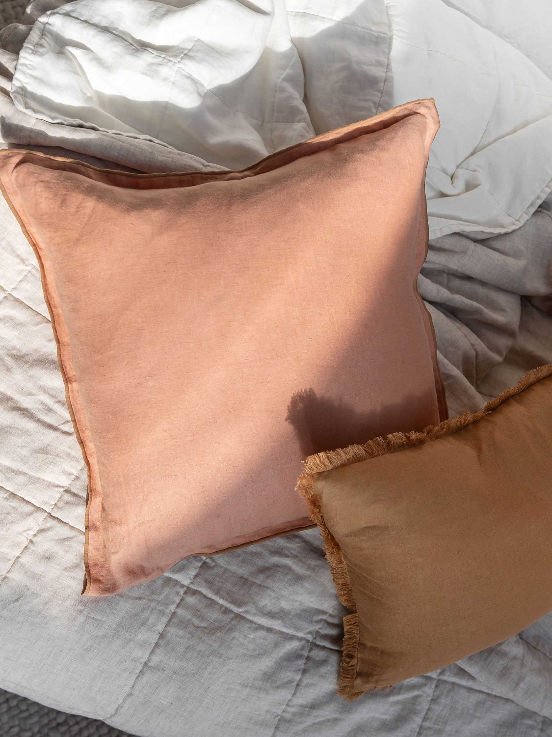 Close up detail of Harlow French Flax linen cushion in Clay colour showing butterscotch overstitching trim and 50cm square size on bed with linen quilt