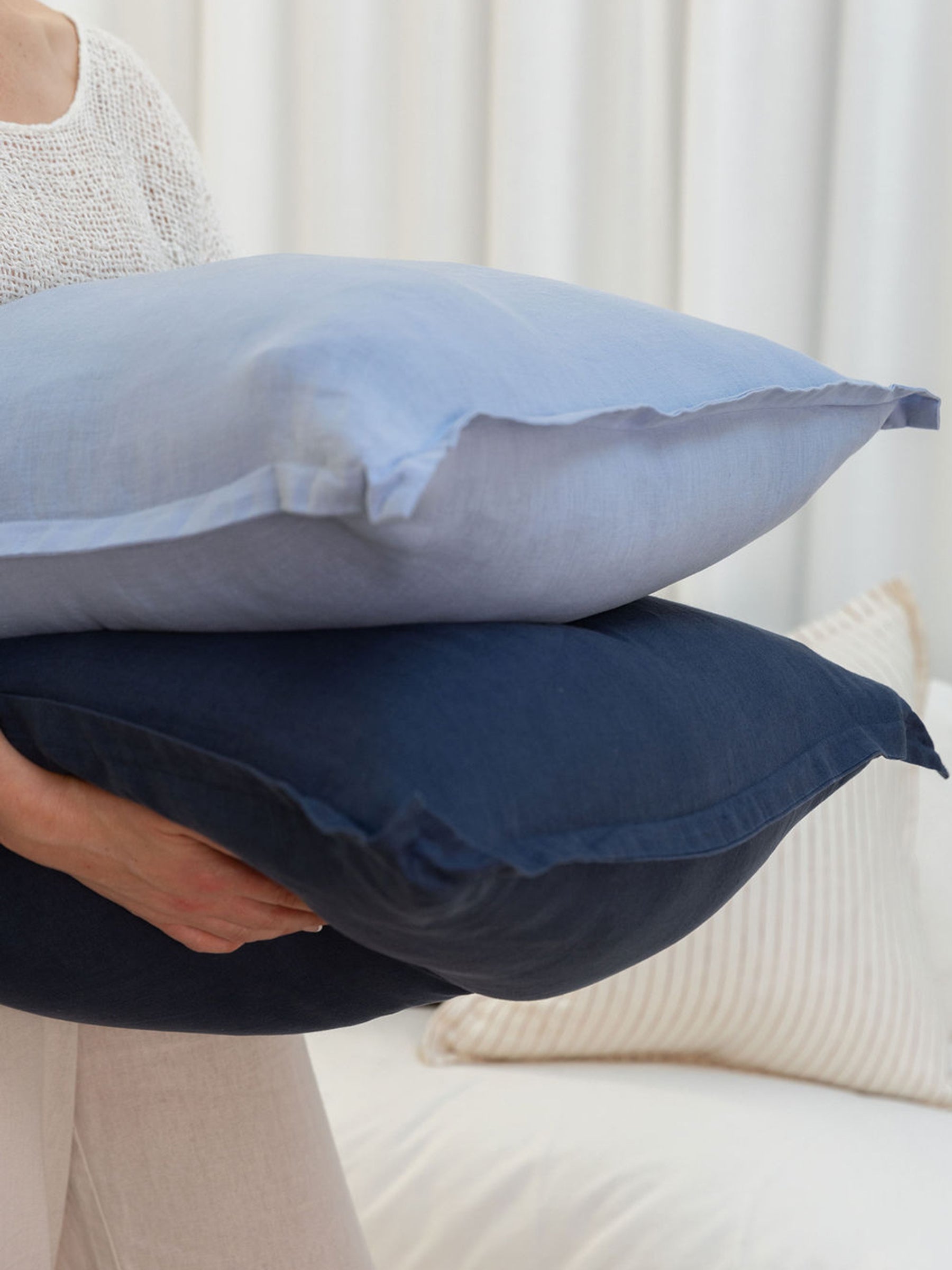 Person holding stacked Reversi® reversible linen flange square cushions showing both sky and navy colors in the set