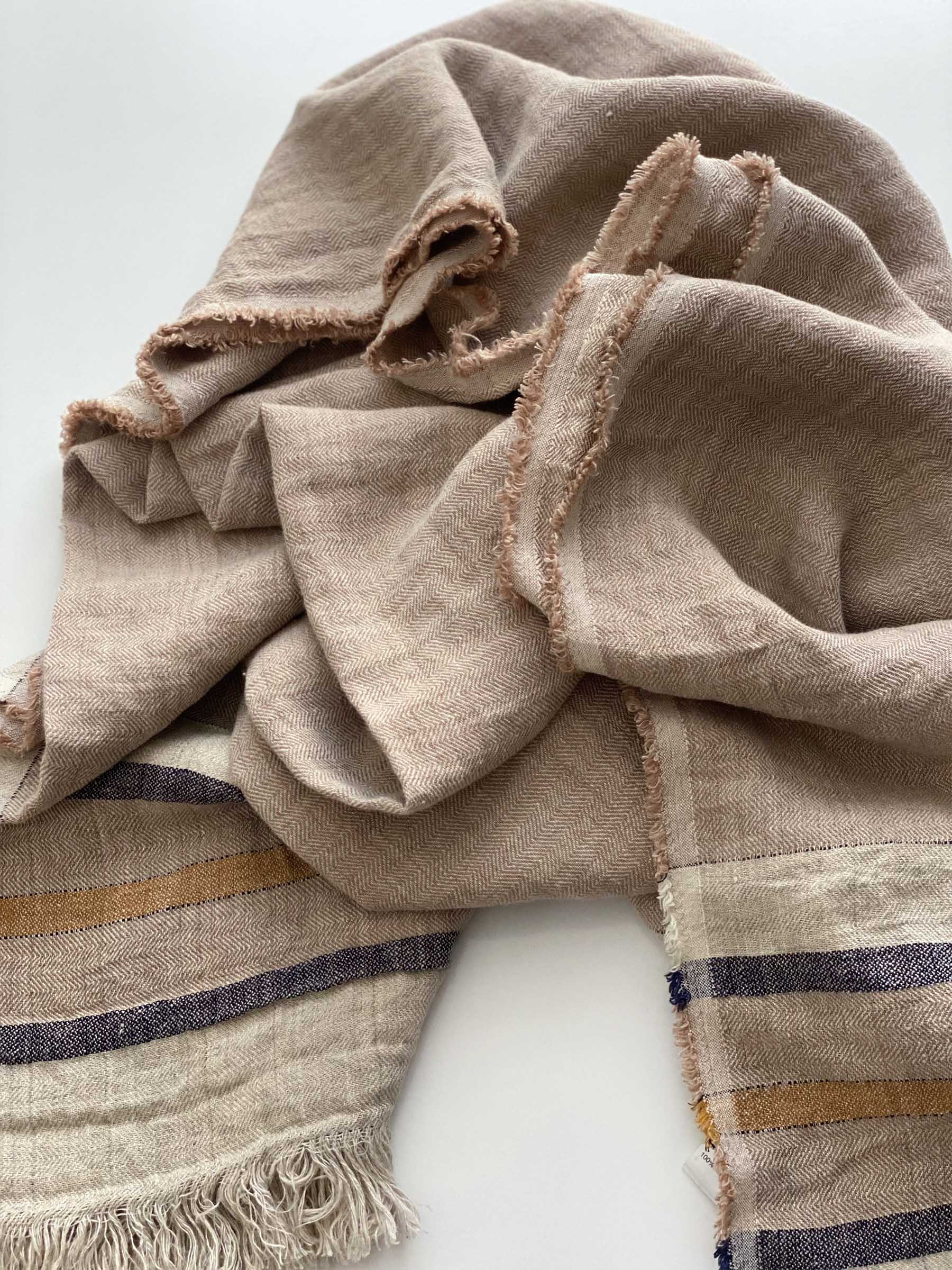 Close-up detail of Arlo french flax linen throw in sand dune colour showing herringbone weave fringed edges and contrasting stripe texture