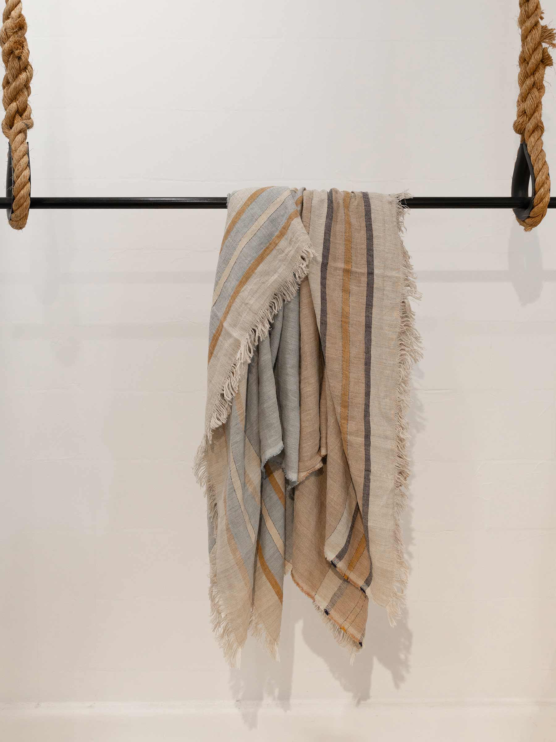 Arlo woven French Flax linen throw collection in all available colours sand dune and seagrass hanging to show fringed edges and contrasting stripe design