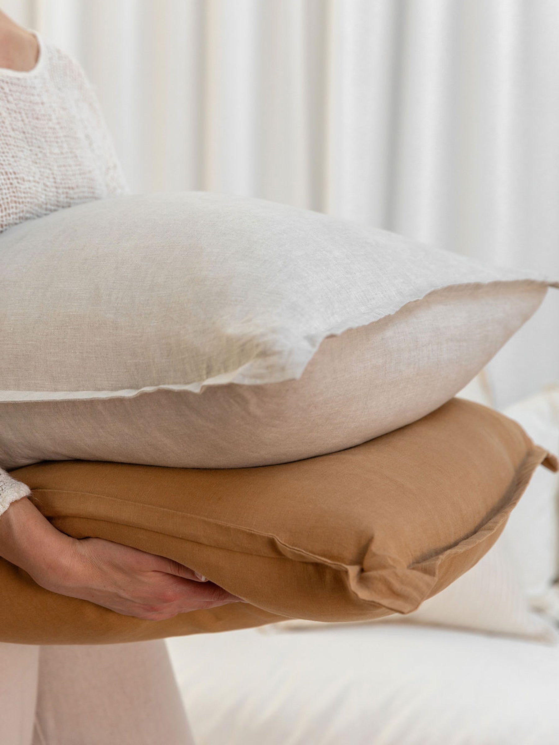 Person holding stacked Reversi® reversible linen flange square cushions showing both natural and butterscotch colours in the set